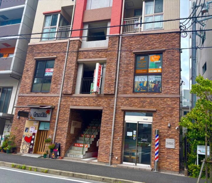 向ヶ丘遊園ねもと整体&ストレッチスタジオが入る茶色いレンガ調の建物。1階に複数の店舗が入居し、2階の窓にオレンジ色の看板が見える