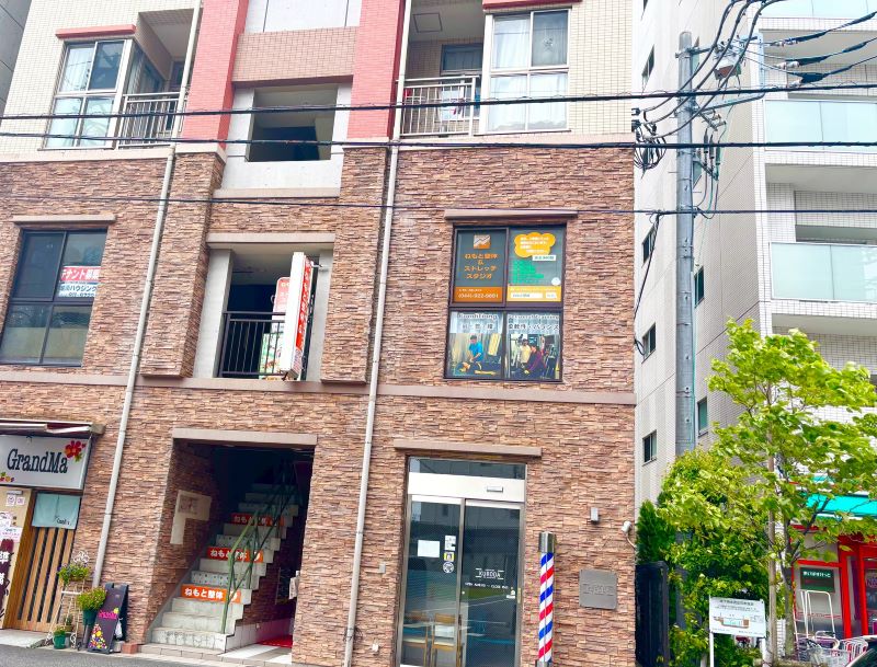 向ヶ丘遊園ねもと整体＆ストレッチスタジオが入る茶色いレンガ調の建物。2階の窓にオレンジ色の看板と施術写真の案内が掲示されている