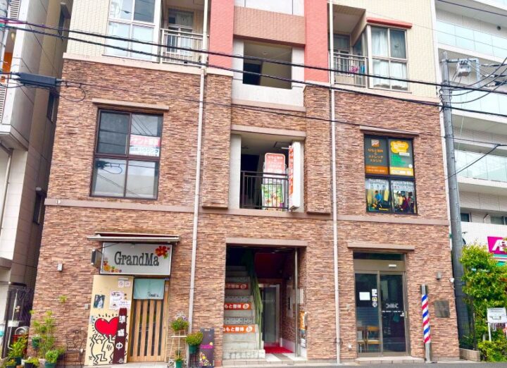 向ヶ丘遊園ねもと整体＆ストレッチスタジオが入る茶色いレンガ調の建物。2階の窓にオレンジ色の看板と施術写真の案内が掲示されている