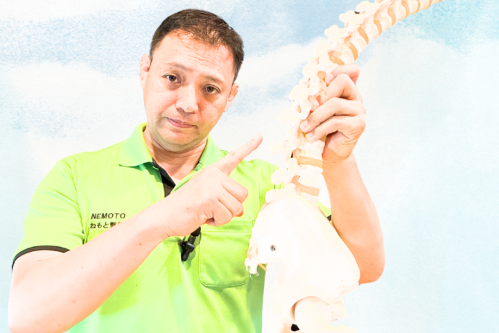 腰椎模型を手に持ち、腰痛の原因を専門的に解説する登戸のねもと整体&ストレッチスタジオ根本大
