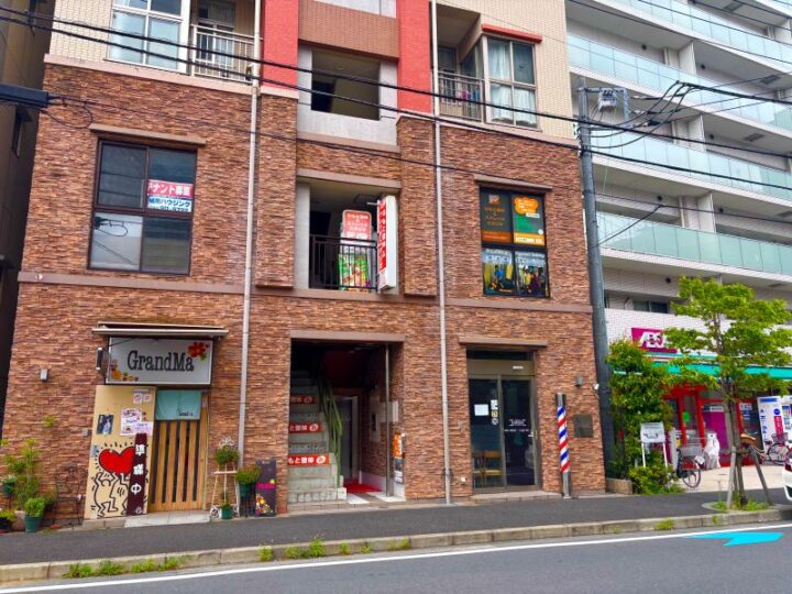 向ヶ丘遊園ねもと整体＆ストレッチスタジオが入る茶色いレンガ調の建物。2階の窓にオレンジ色の看板と施術写真の案内が掲示されている