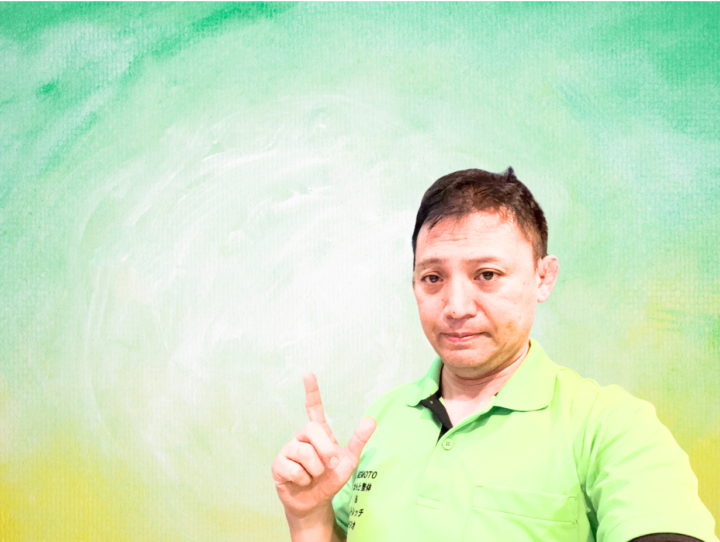 整体師が首の神経の問題について説明している様子。緑色の背景に立ち、指でポイントを示している男性。首や肩の不調、神経症状についての健康アドバイスを伝える場面