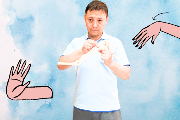 腕や手の関節イラストと骨模型を持って説明する整体師の写真